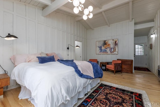 bedroom with lofted ceiling with beams, an inviting chandelier, a decorative wall, and light wood finished floors