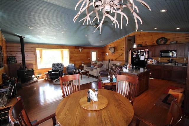 dining area with wooden walls, wood finished floors, lofted ceiling, a wood stove, and wood ceiling