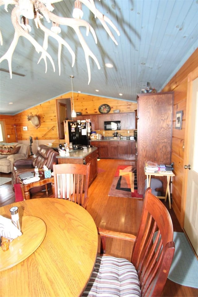 dining space featuring lofted ceiling, light wood-style floors, wood walls, and wooden ceiling