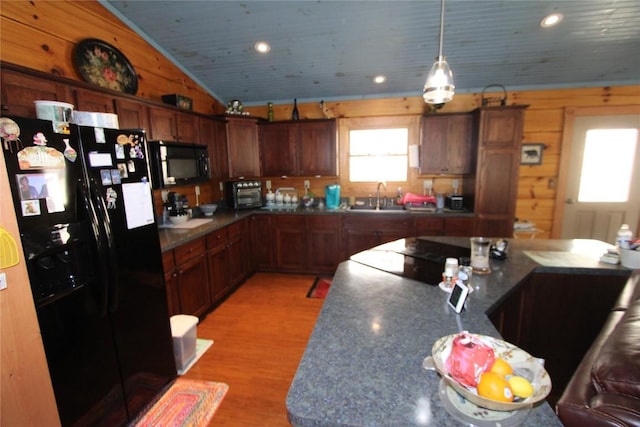 kitchen featuring wood walls, lofted ceiling, light wood-style flooring, black appliances, and a sink