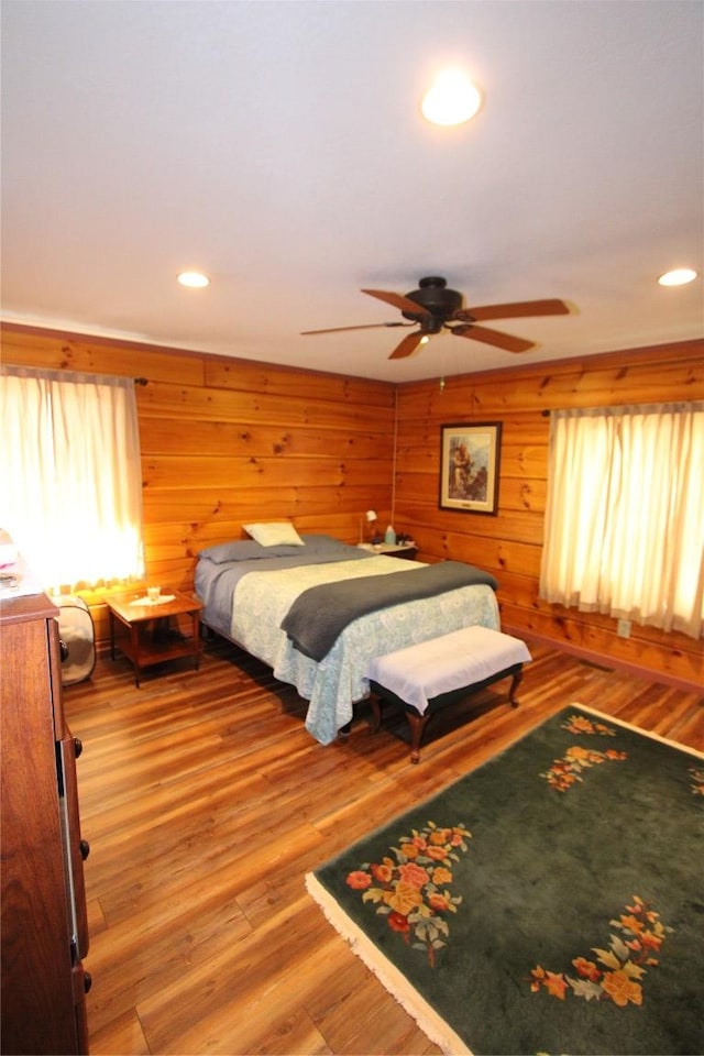 bedroom with recessed lighting, a ceiling fan, wood walls, and wood finished floors