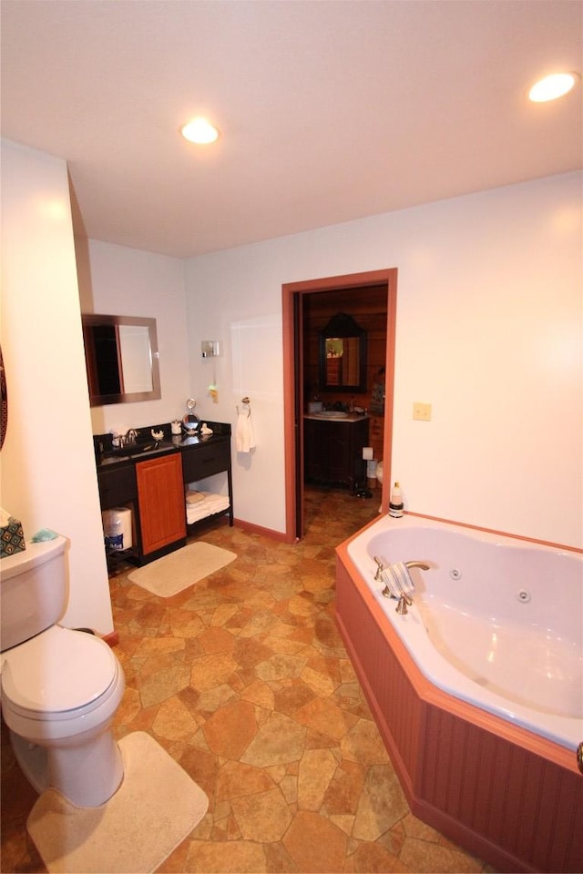 bathroom with vanity, toilet, a tub with jets, and recessed lighting