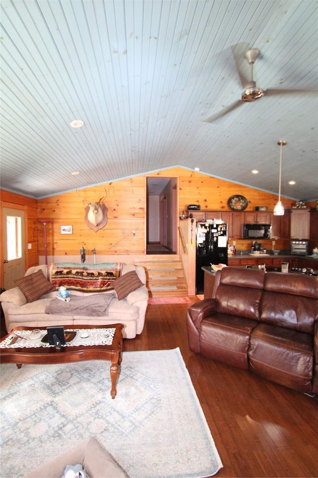 living room featuring lofted ceiling, wooden walls, wood finished floors, and stairs