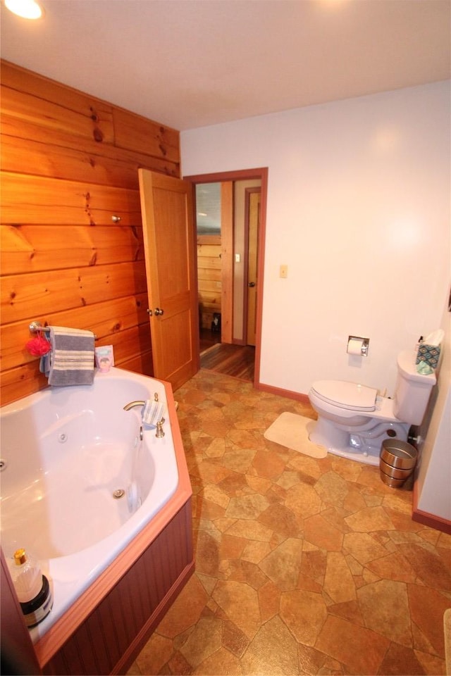 full bathroom with toilet, stone finish floor, a jetted tub, wooden walls, and baseboards