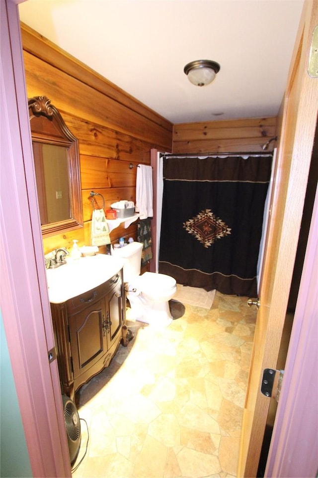 bathroom featuring wood walls, curtained shower, vanity, and toilet