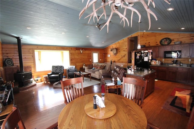 dining area with wood finished floors, wooden ceiling, wood walls, lofted ceiling, and a wood stove