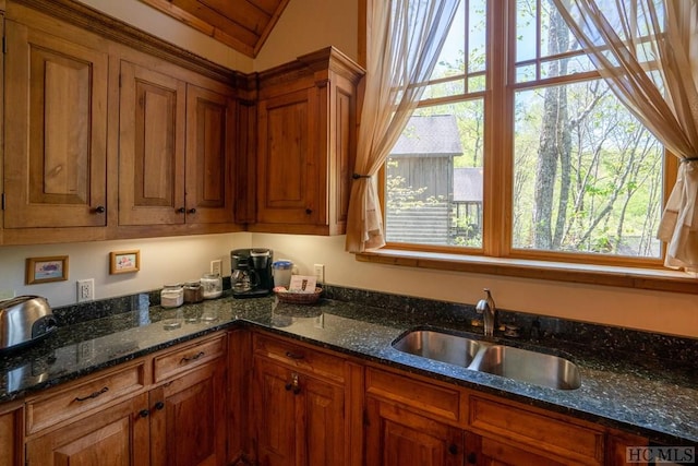 kitchen with vaulted ceiling, sink, and dark stone counters