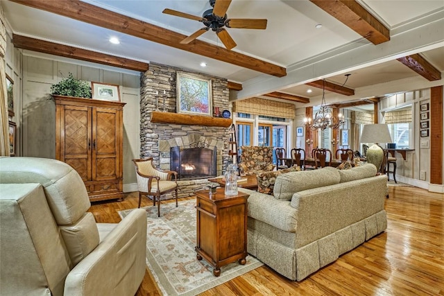 living room featuring ceiling fan with notable chandelier, a fireplace, baseboards, light wood-type flooring, and beam ceiling