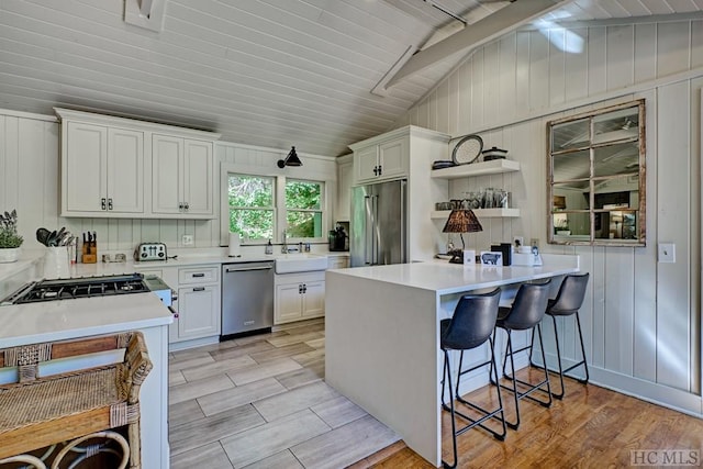 kitchen featuring light wood-type flooring, vaulted ceiling, appliances with stainless steel finishes, white cabinets, and a breakfast bar area