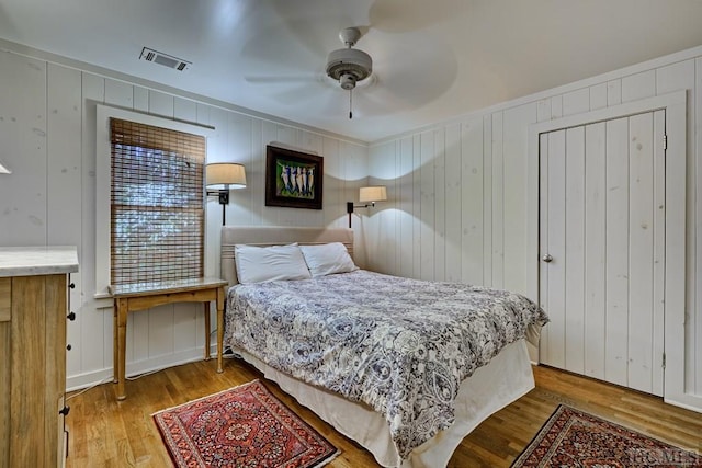 bedroom featuring ceiling fan, a decorative wall, visible vents, and wood finished floors