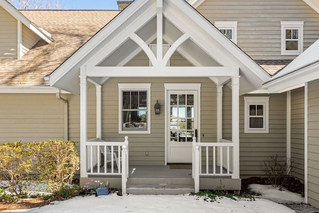 snow covered property entrance featuring roof with shingles and a chimney