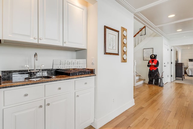 kitchen with a sink, light wood-style flooring, dark stone countertops, white cabinetry, and baseboards