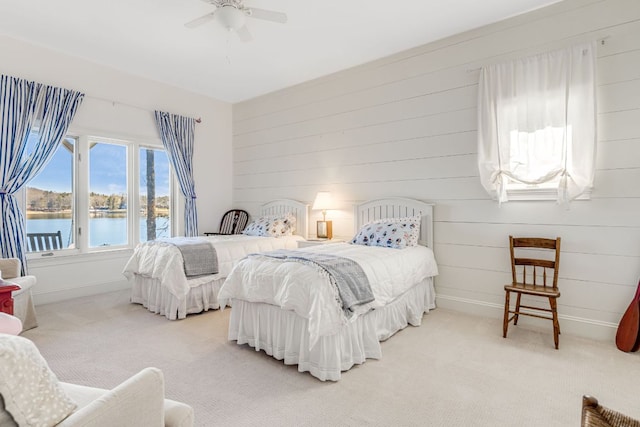 bedroom featuring light colored carpet, a water view, ceiling fan, wood walls, and baseboards