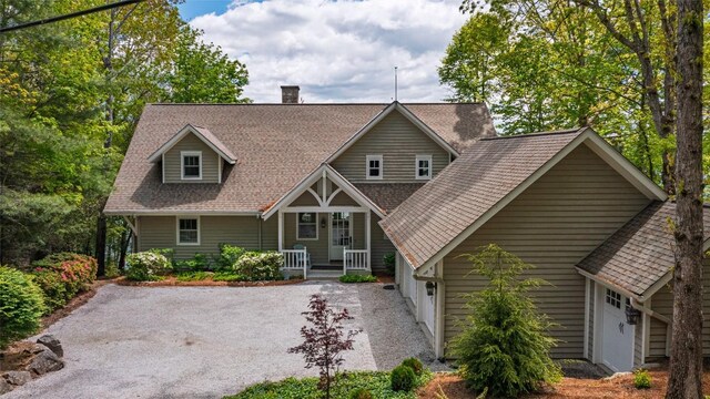 view of front facade featuring covered porch, a garage, a chimney, driveway, and a shingled roof