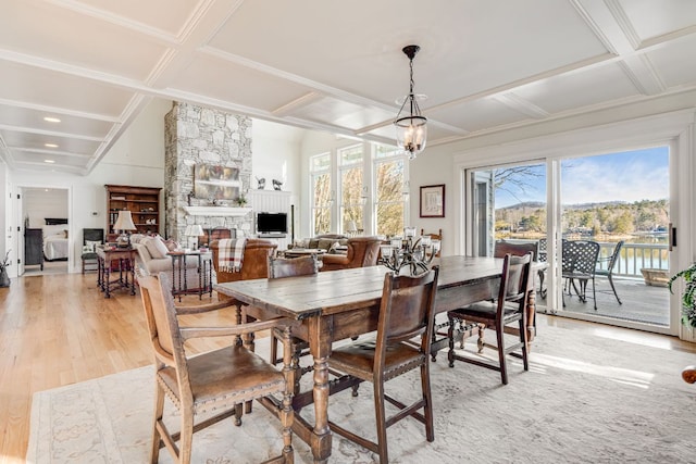 dining room with coffered ceiling, light wood-style flooring, a stone fireplace, beam ceiling, and a chandelier