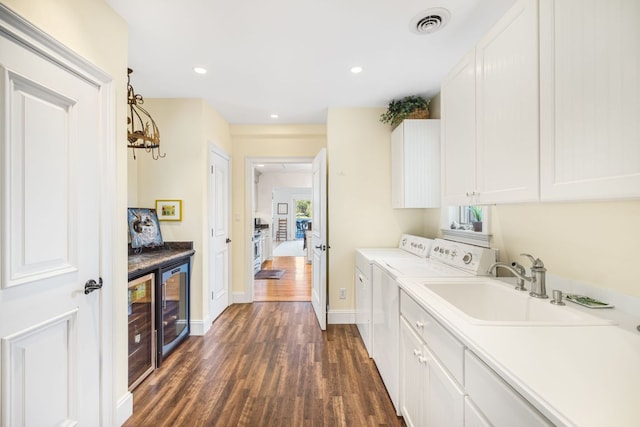 clothes washing area with washing machine and clothes dryer, cabinet space, dark wood-type flooring, beverage cooler, and baseboards