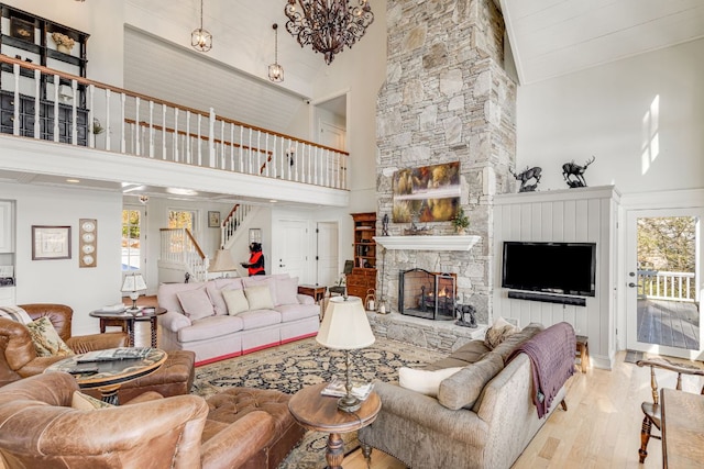 living room with a high ceiling, wood finished floors, plenty of natural light, stairs, and a stone fireplace