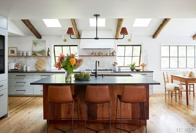 kitchen featuring a center island with sink, beamed ceiling, and tasteful backsplash