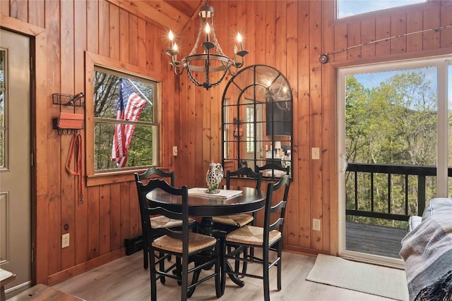 dining space with wooden walls, a chandelier, wood finished floors, and baseboards