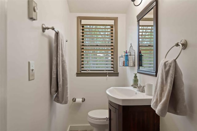 half bath featuring plenty of natural light, baseboards, vanity, and toilet