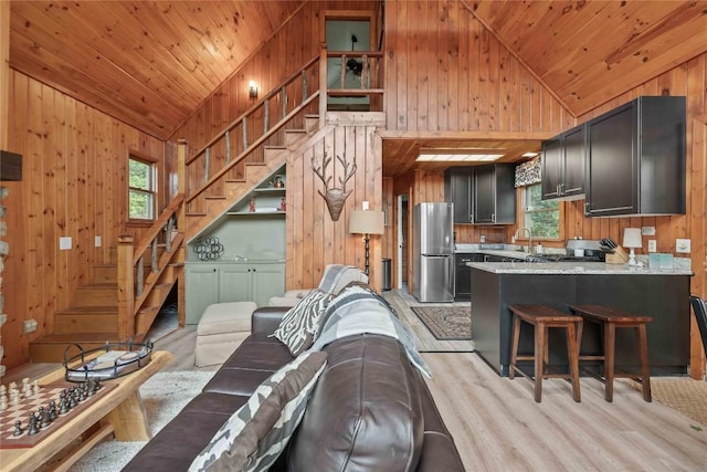 living room featuring wood walls, light wood finished floors, plenty of natural light, stairs, and wooden ceiling