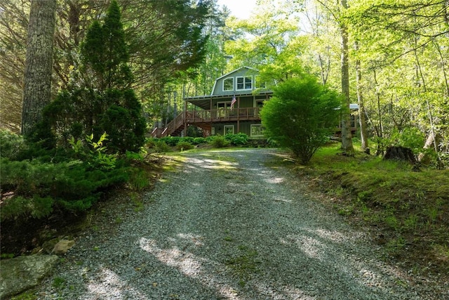 view of front facade with stairway, driveway, a view of trees, and a porch