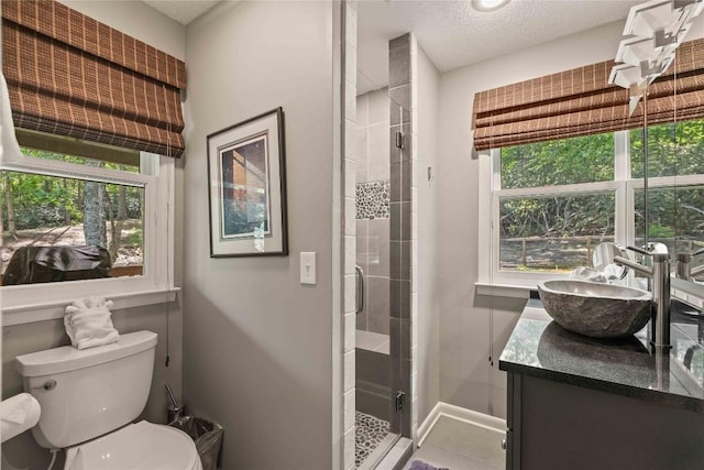 full bath featuring a stall shower, toilet, vanity, baseboards, and a textured ceiling