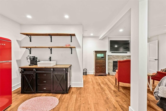 bar featuring a sink, light wood-style floors, a fireplace, baseboards, and recessed lighting
