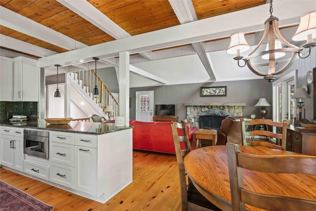 kitchen featuring beamed ceiling, white cabinets, decorative backsplash, light wood finished floors, and a stone fireplace