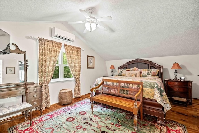 bedroom with a wall unit AC, a textured ceiling, vaulted ceiling, wood finished floors, and ceiling fan