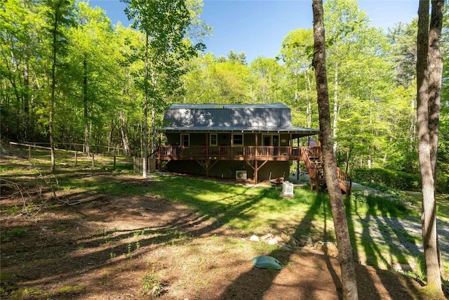 back of property with a view of trees, a wooden deck, stairs, metal roof, and a lawn