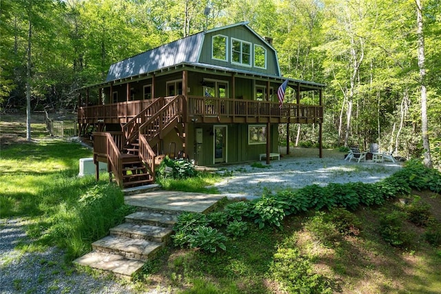 rear view of property with a gambrel roof, a forest view, a wooden deck, and stairway