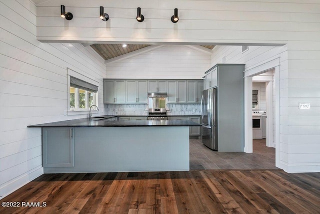 kitchen with vaulted ceiling with beams, stove, kitchen peninsula, stainless steel fridge, and sink