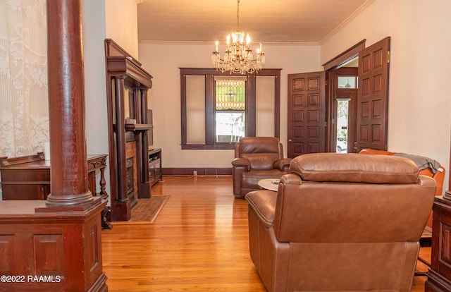 living room featuring an inviting chandelier, decorative columns, ornamental molding, and light wood-type flooring