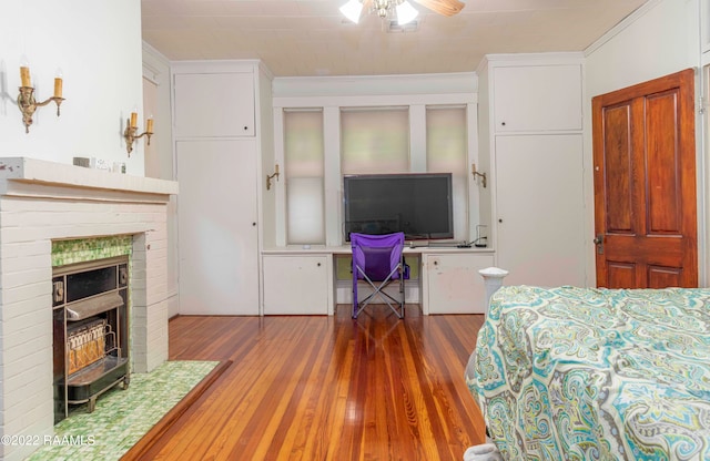 bedroom with crown molding, a brick fireplace, ceiling fan, and dark wood-type flooring