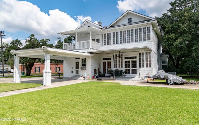 back of house with a balcony, a lawn, and a carport