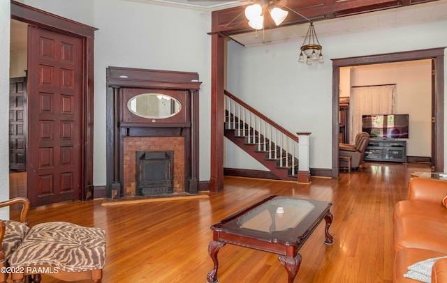 living room with a brick fireplace, ornamental molding, wood-type flooring, and ceiling fan with notable chandelier