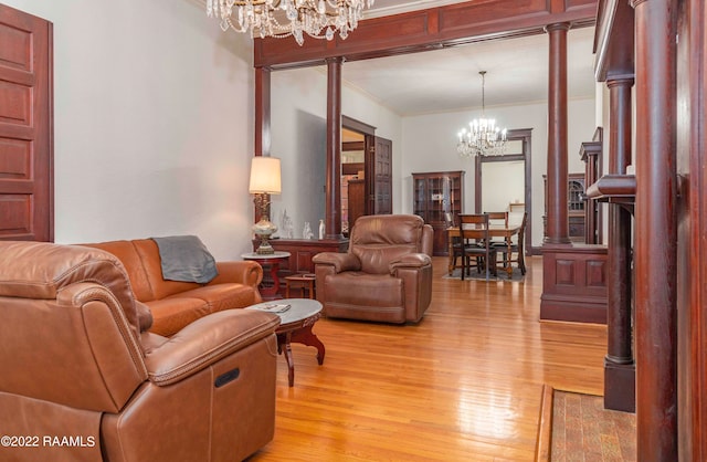 living room with crown molding, light hardwood / wood-style flooring, a chandelier, and decorative columns