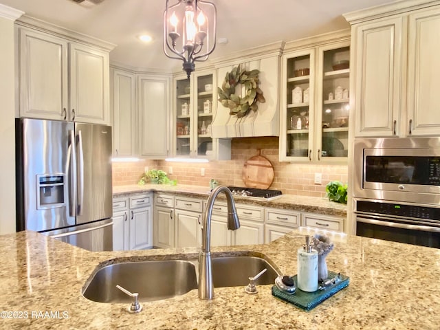 kitchen with a notable chandelier, appliances with stainless steel finishes, light stone counters, tasteful backsplash, and pendant lighting