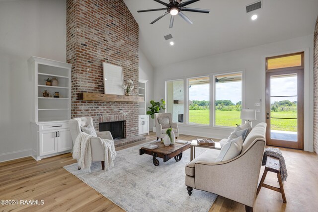 living room featuring a fireplace, light hardwood / wood-style floors, high vaulted ceiling, and ceiling fan