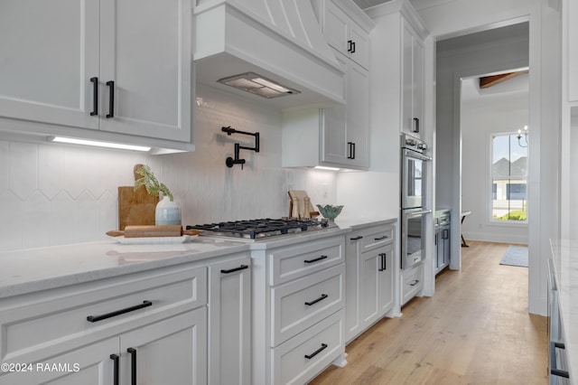 kitchen featuring decorative backsplash, custom exhaust hood, stainless steel appliances, light hardwood / wood-style flooring, and white cabinetry