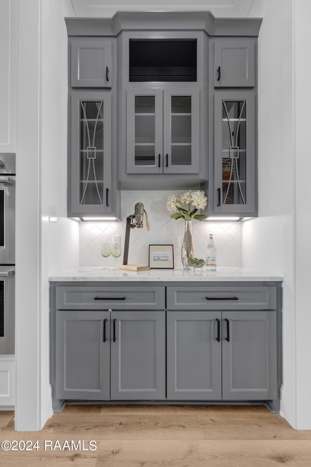 bar featuring light wood-type flooring, gray cabinets, and tasteful backsplash