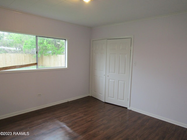 unfurnished bedroom with a closet, dark hardwood / wood-style flooring, and crown molding