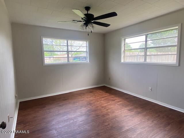 unfurnished room featuring ceiling fan, dark wood-type flooring, and a healthy amount of sunlight