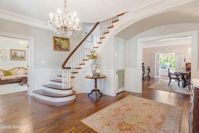 stairs featuring an inviting chandelier, ornamental molding, and dark hardwood / wood-style floors