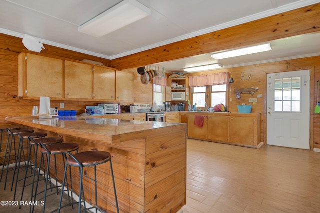 kitchen with wood walls, stainless steel electric range oven, ornamental molding, and a kitchen breakfast bar