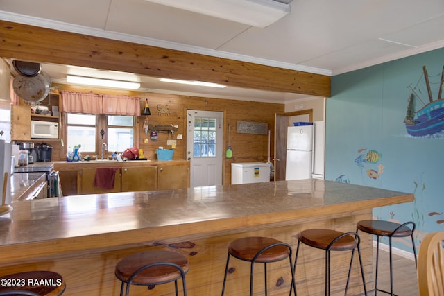 kitchen with a breakfast bar, white appliances, wood walls, kitchen peninsula, and hardwood / wood-style flooring