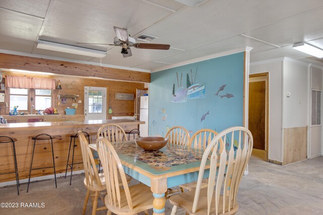 dining room featuring ceiling fan, bar area, and wood walls