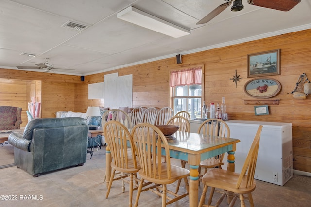 dining area with wood walls, ceiling fan, and crown molding