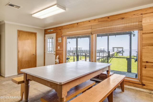 dining area featuring light tile flooring, a water view, wood walls, and a wealth of natural light